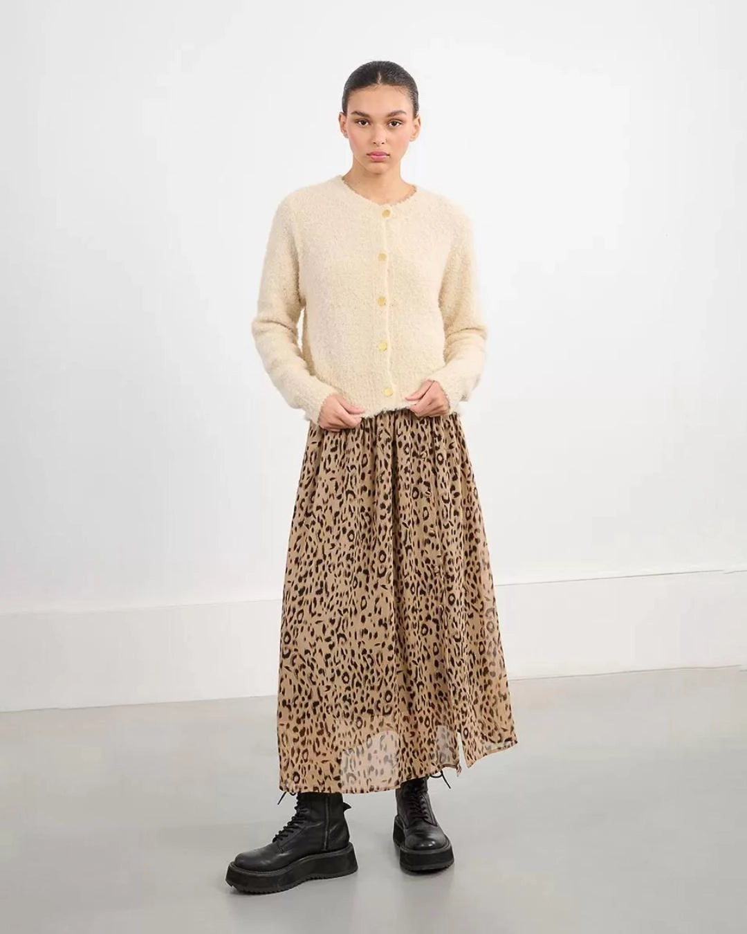 Woman wearing a beige fluffy cardigan with gold buttons and cheetah skirt