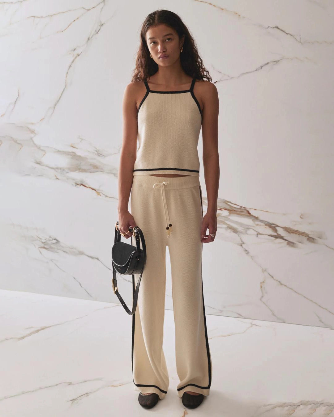 Woman wearing a beige tank top and pants with black trim and matching pants