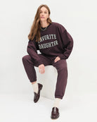 Woman wearing a maroon 'FAVORITE DAUGHTER' sweatshirt and matching sweatpants