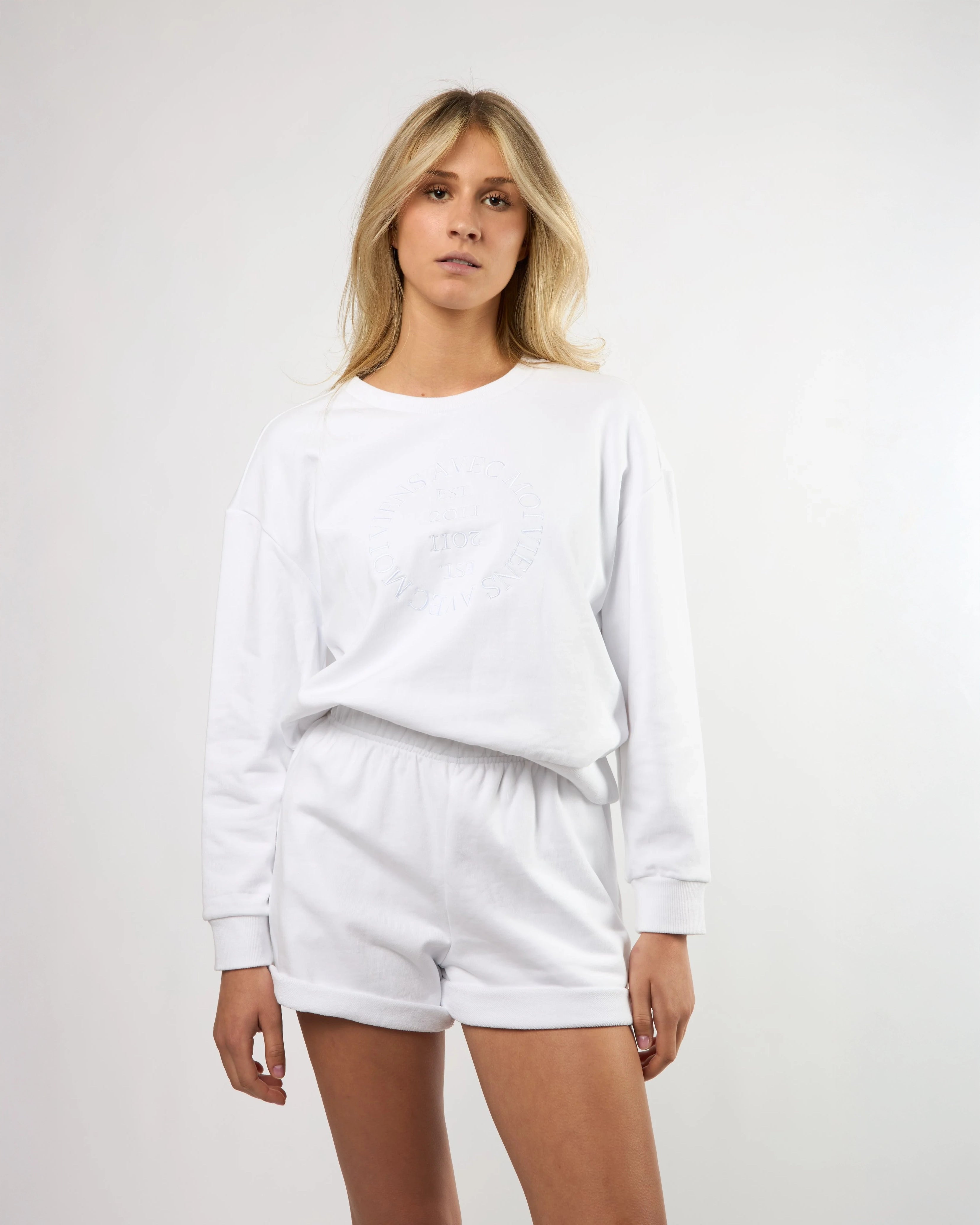 woman wearing a white crew neck sweatshirt and matching shorts with embroidery on the chest