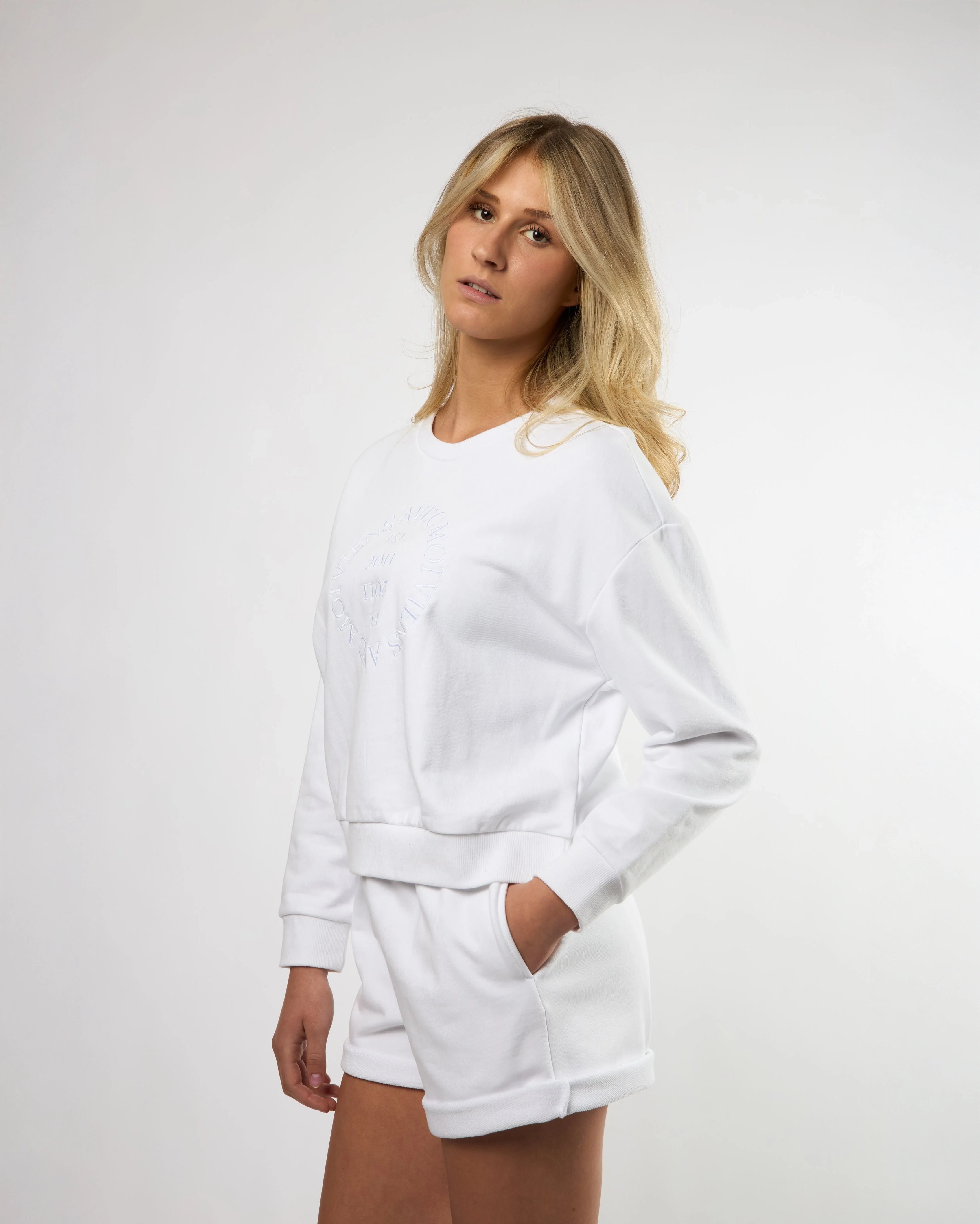 woman wearing a white crew neck sweatshirt and matching shorts with embroidery on the chest