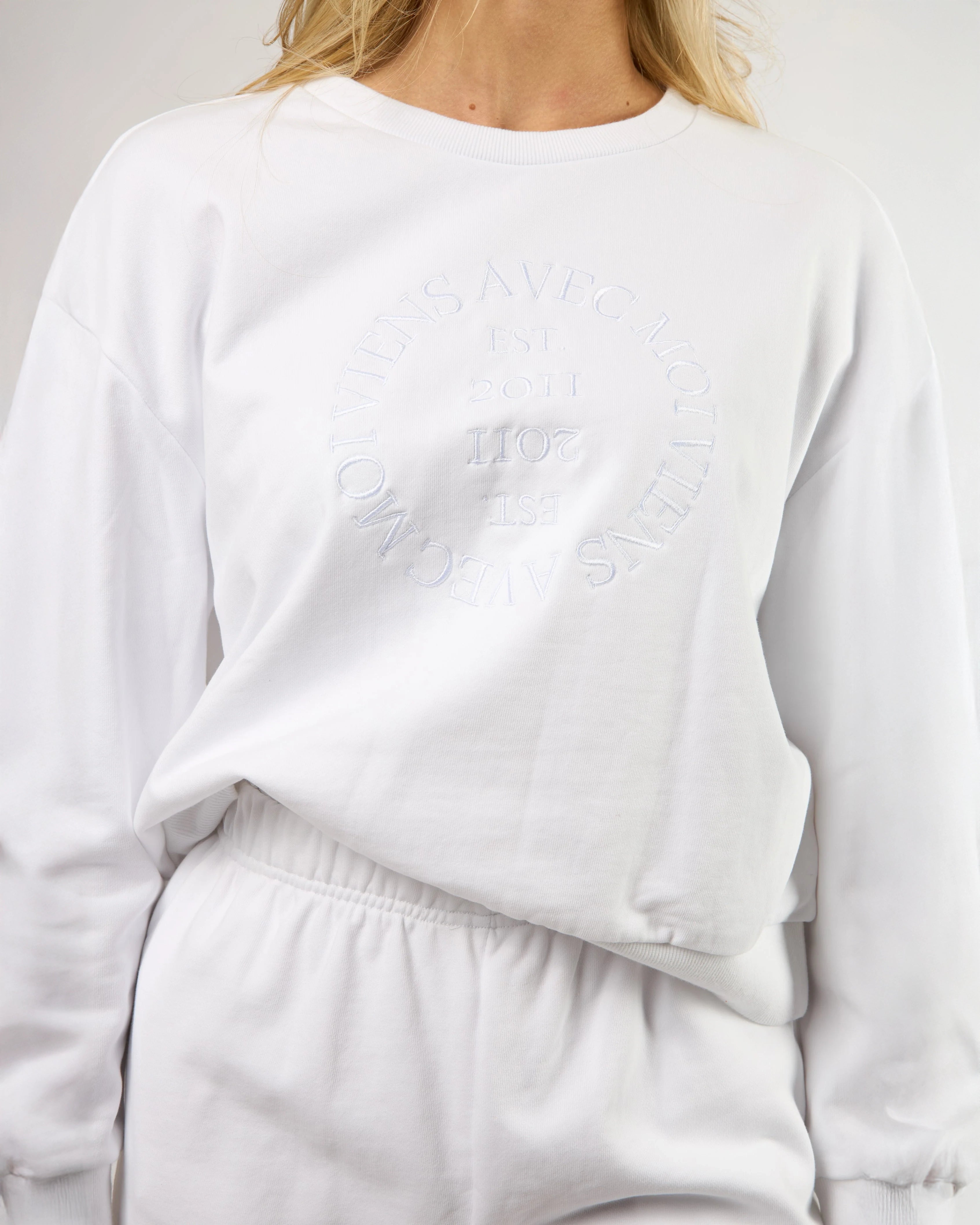 woman wearing a white crew neck sweatshirt with embroidery on the chest