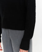 a woman wears a black ribbed knit sweater
