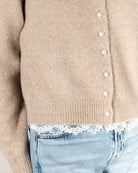 beige knit cardigan with pearl buttons and lace trim on the bottom