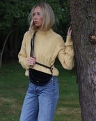 Woman in a yellow cable knit sweater standing next to a tree 