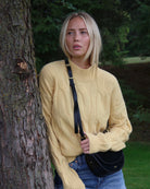 Woman in a yellow cable knit sweater standing next to a tree 