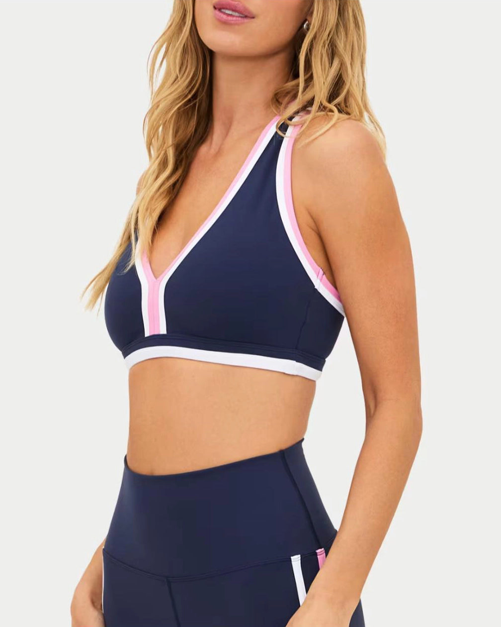 a woman wears a navy racerback sports bra with pink and white outline