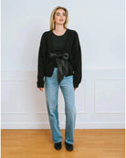 Woman wearing a black cardigan over a black turtleneck with a large black satin bow