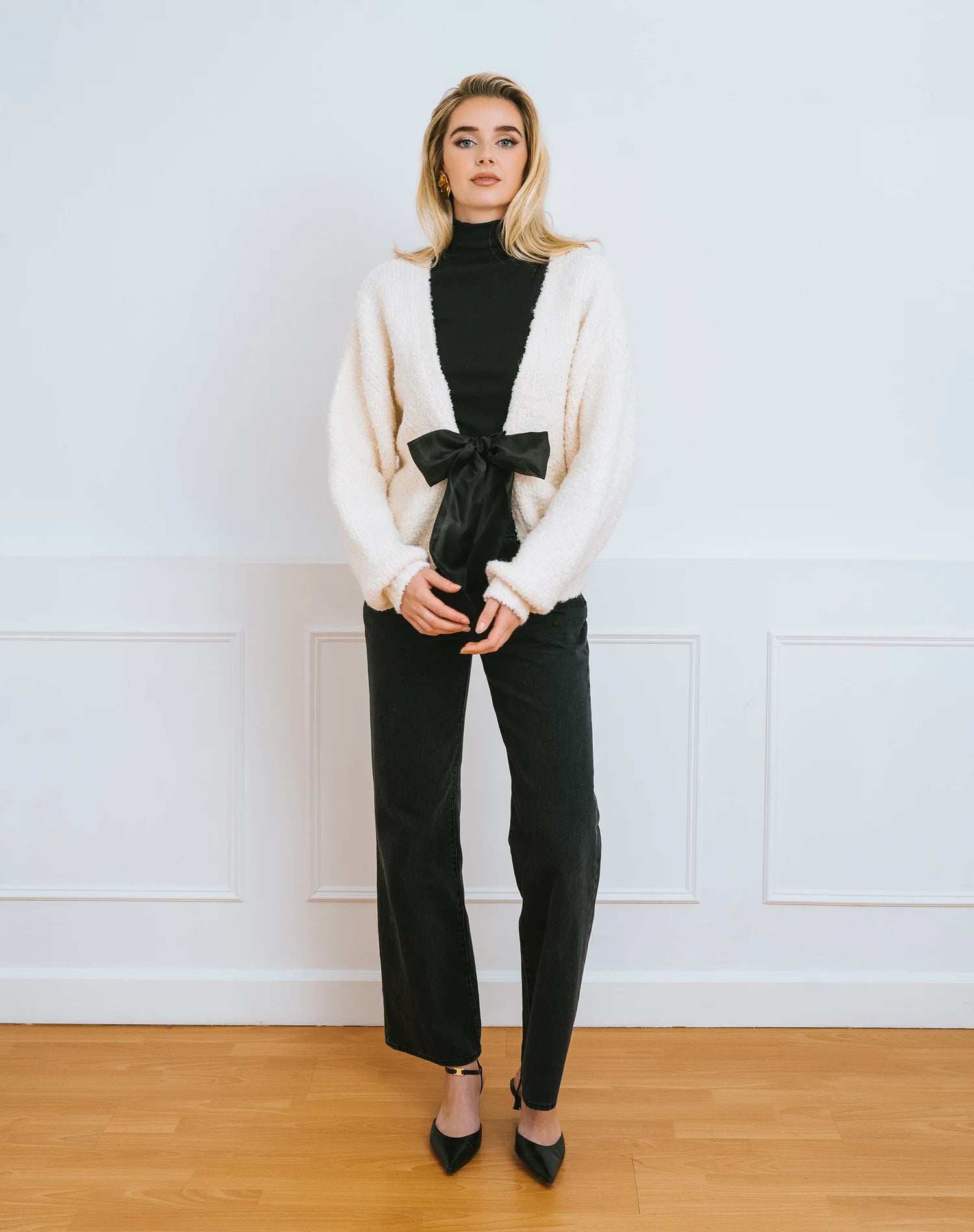 Woman wearing a cream cardigan over a black turtleneck with a large black satin bow
