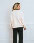 Woman wearing a cream cardigan over a black turtleneck with a large black satin bow