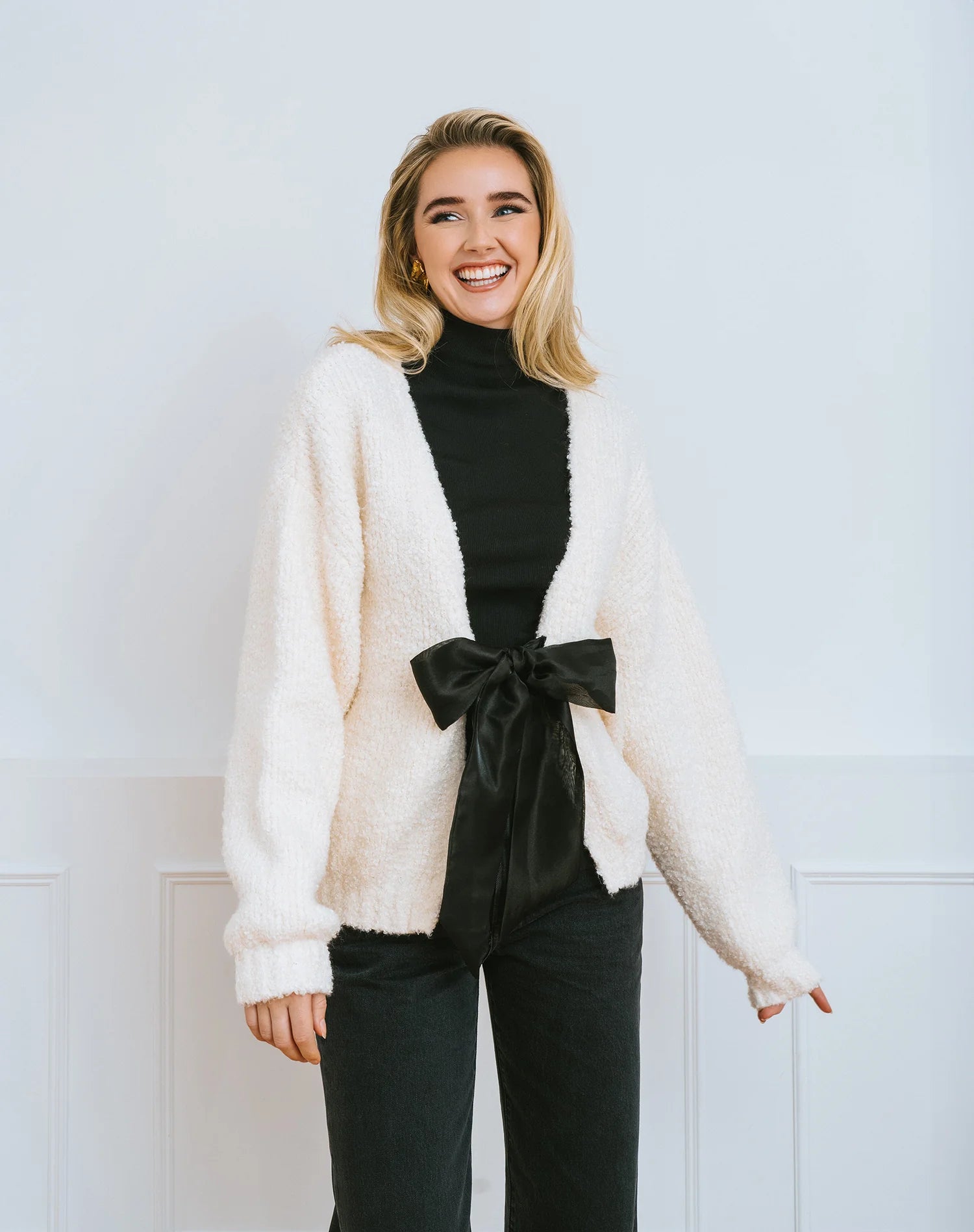 Woman wearing a cream cardigan over a black turtleneck with a large black satin bow