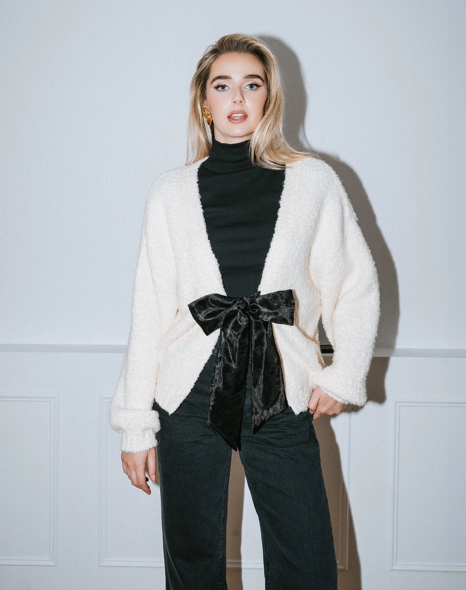 Woman wearing a cream cardigan over a black turtleneck with a large black satin bow