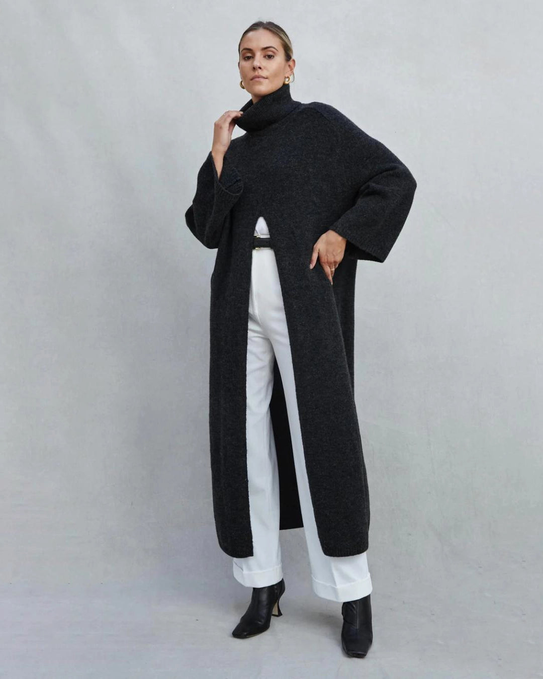 Woman wearing a long turtleneck sweater dress in black with a large slit up the front