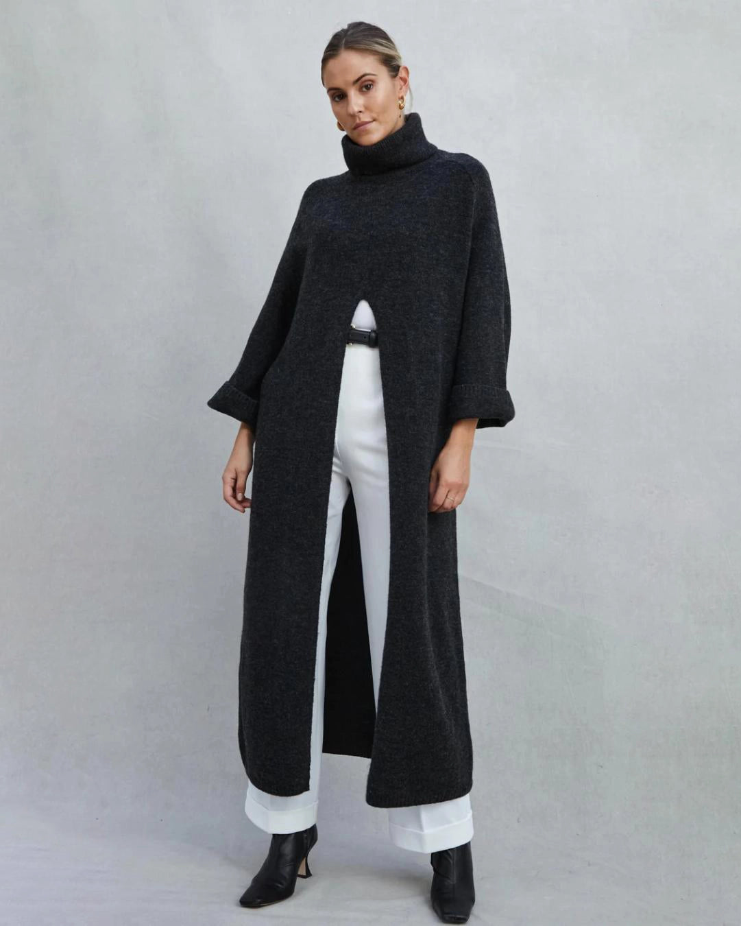 Woman wearing a long turtleneck sweater dress in black with a large slit up the front