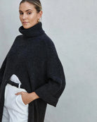 Woman wearing a long turtleneck sweater dress in black with a large slit up the front