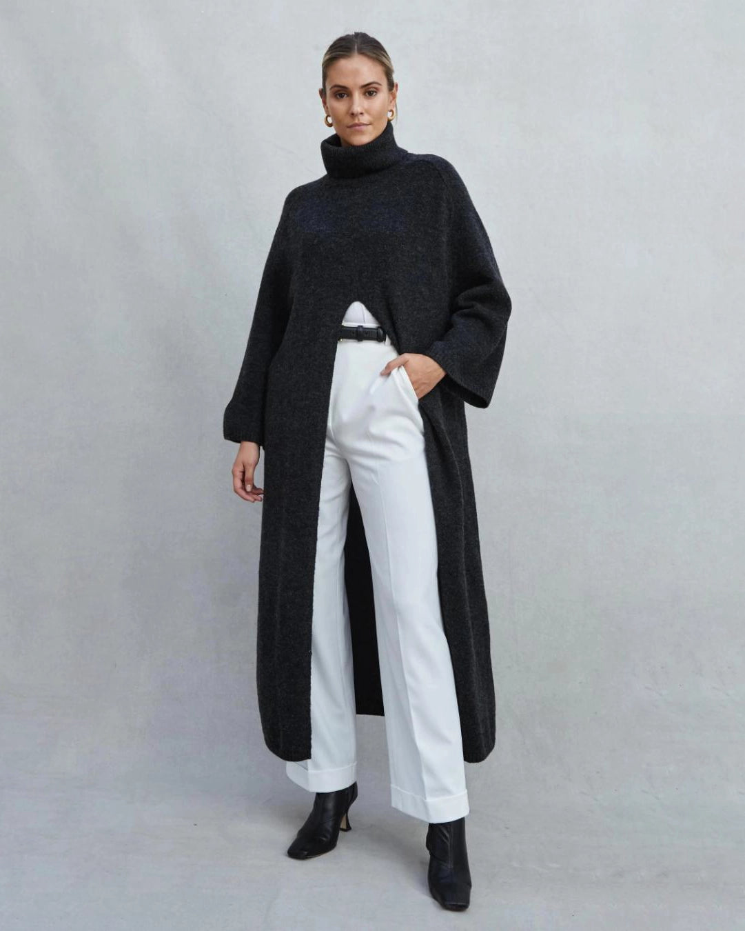 Woman wearing a long turtleneck sweater dress in black with a large slit up the front