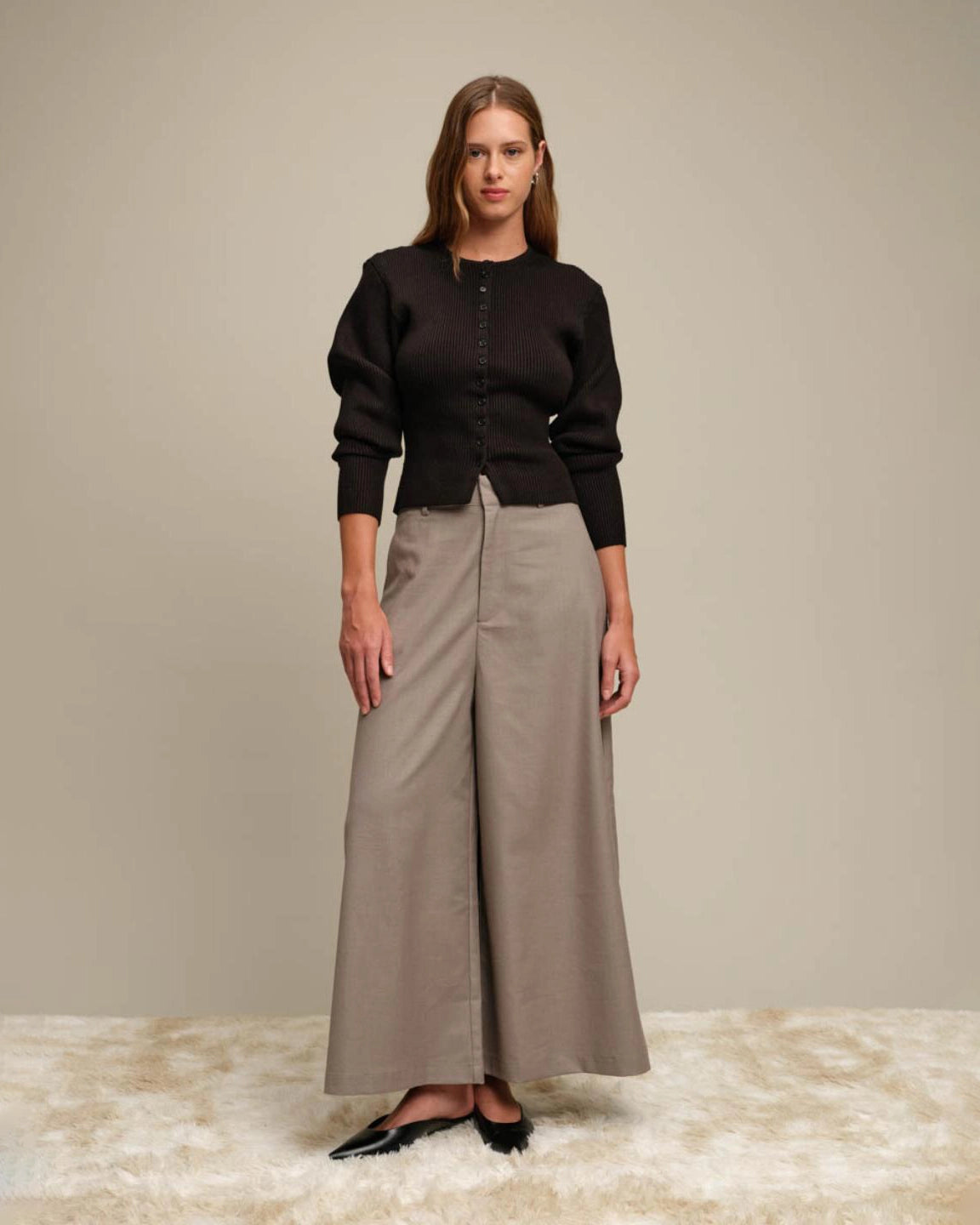 Woman wearing a black ribbed button down cardigan and beige wide-leg pants