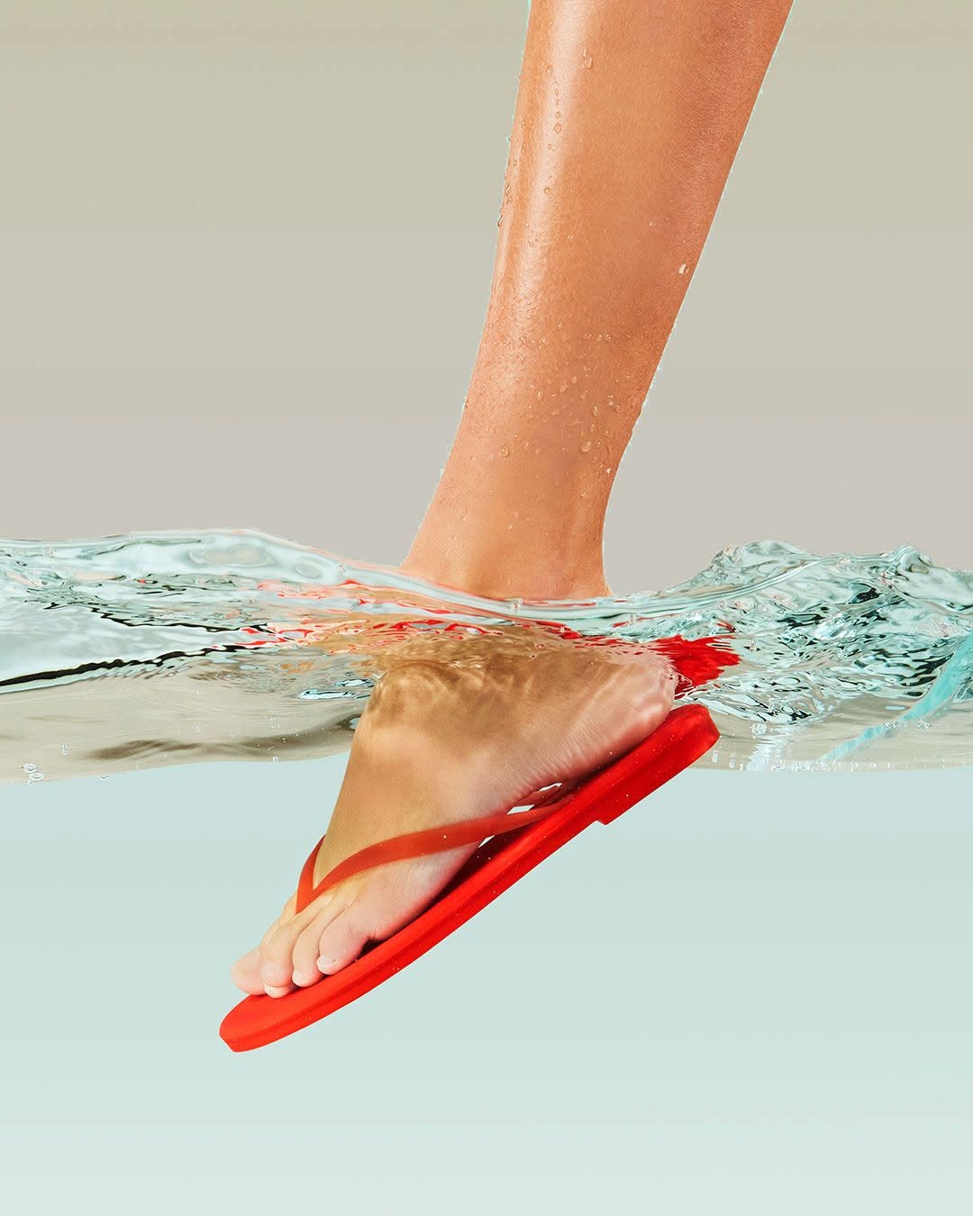 A red flip-flop sandal worn on a person's foot, shown with water splashing around the foot and sandal against a light gray background.