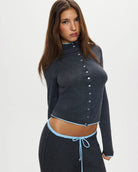 Woman wearing a dark gray button-up ribbed top in dark grey with a pale blue trim