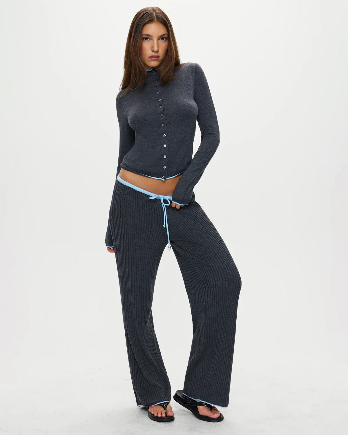 Woman wearing a dark gray button-up ribbed top in dark grey with a pale blue trim and matching pants