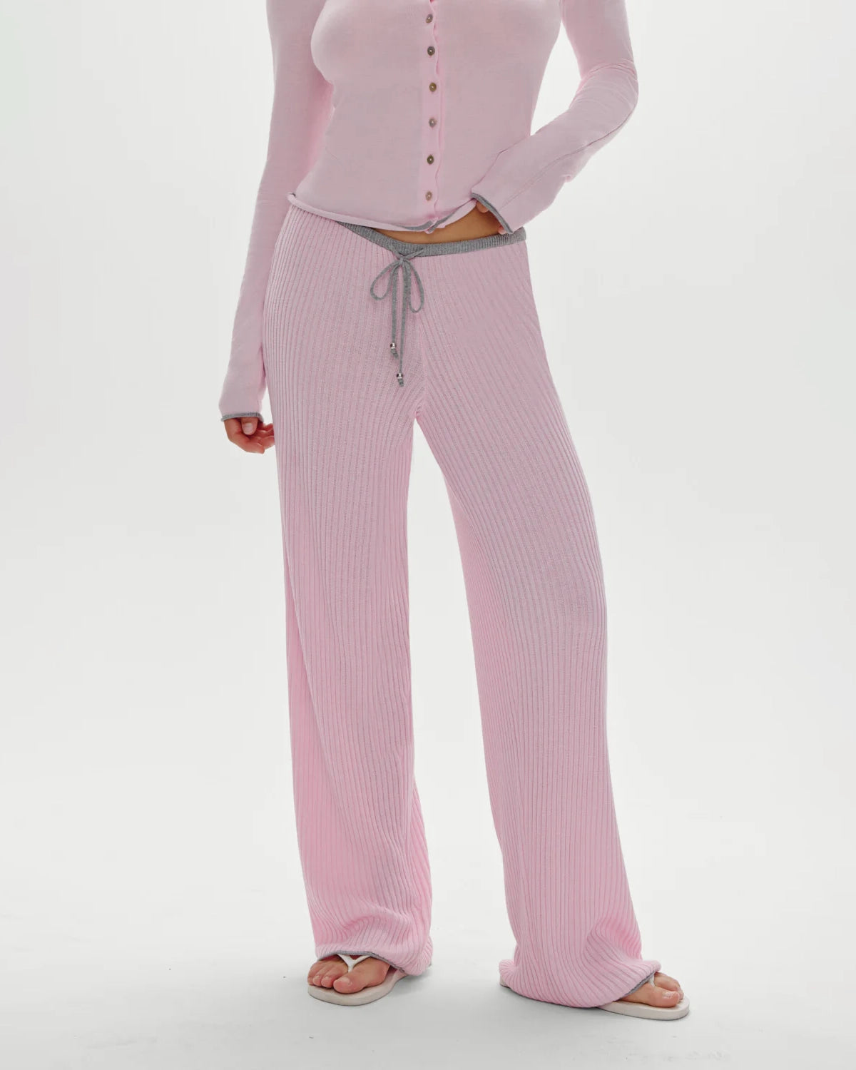 A woman wearing a pink ribbed lounge pant with grey drawstring and trim
