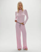 A woman wearing a pink ribbed lounge pant and top with grey drawstring and trim