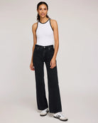 Woman wearing a white tank top with black trim and dark jeans