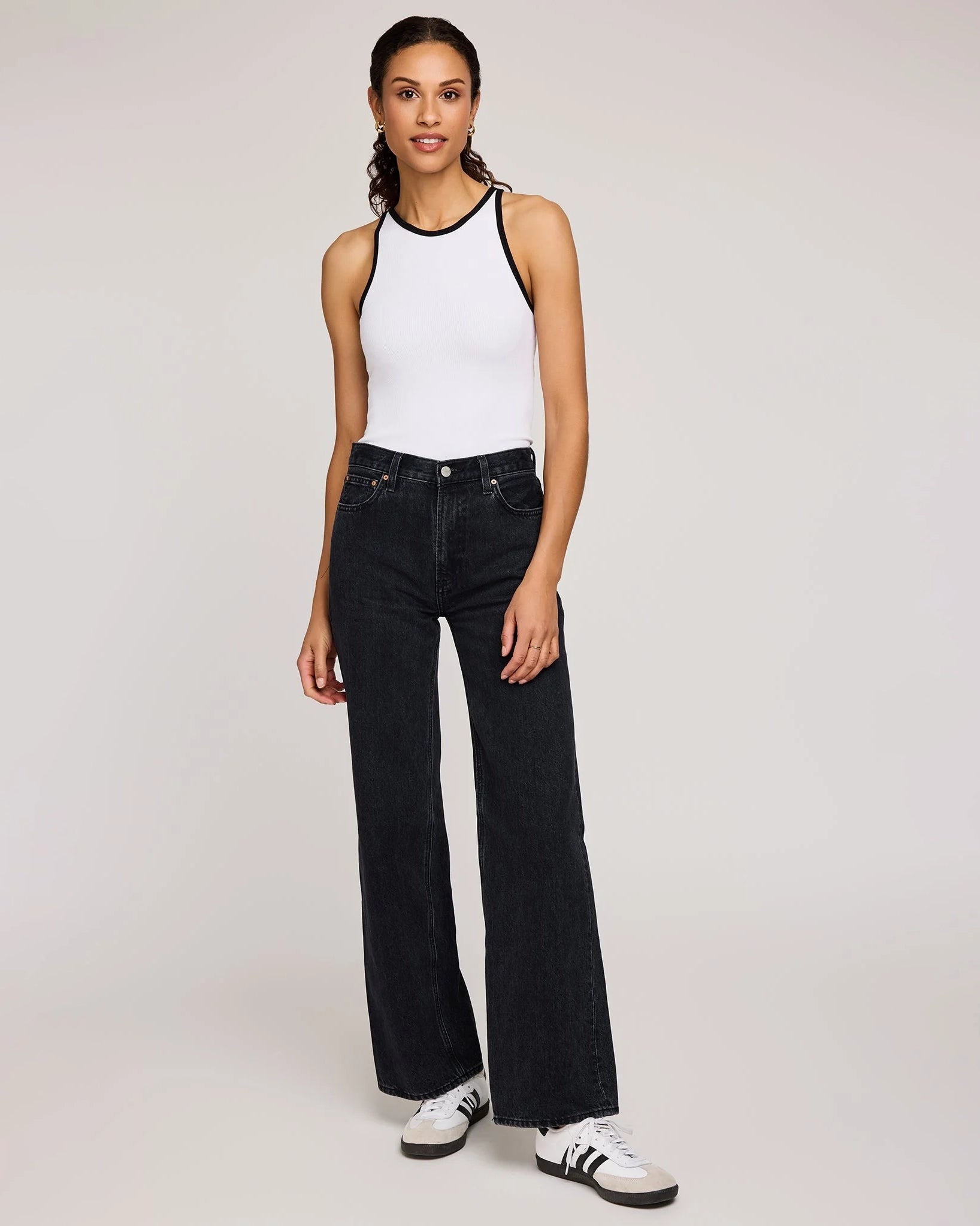 Woman wearing a white tank top with black trim and dark jeans