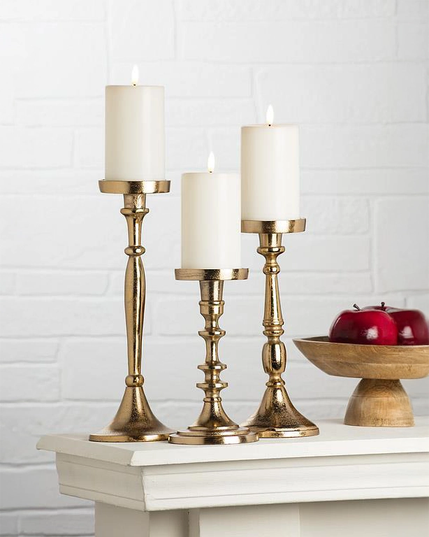 three gold candle holders with pillar candles in 3 different sizes: small, medium and large on mantle