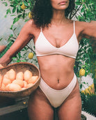 woman wearing a beige bralatte and undies sitting with a basket of oranges and lemons in a garden setting