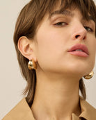 A woman wears a pair of gold statement earrings by Jenny Bird