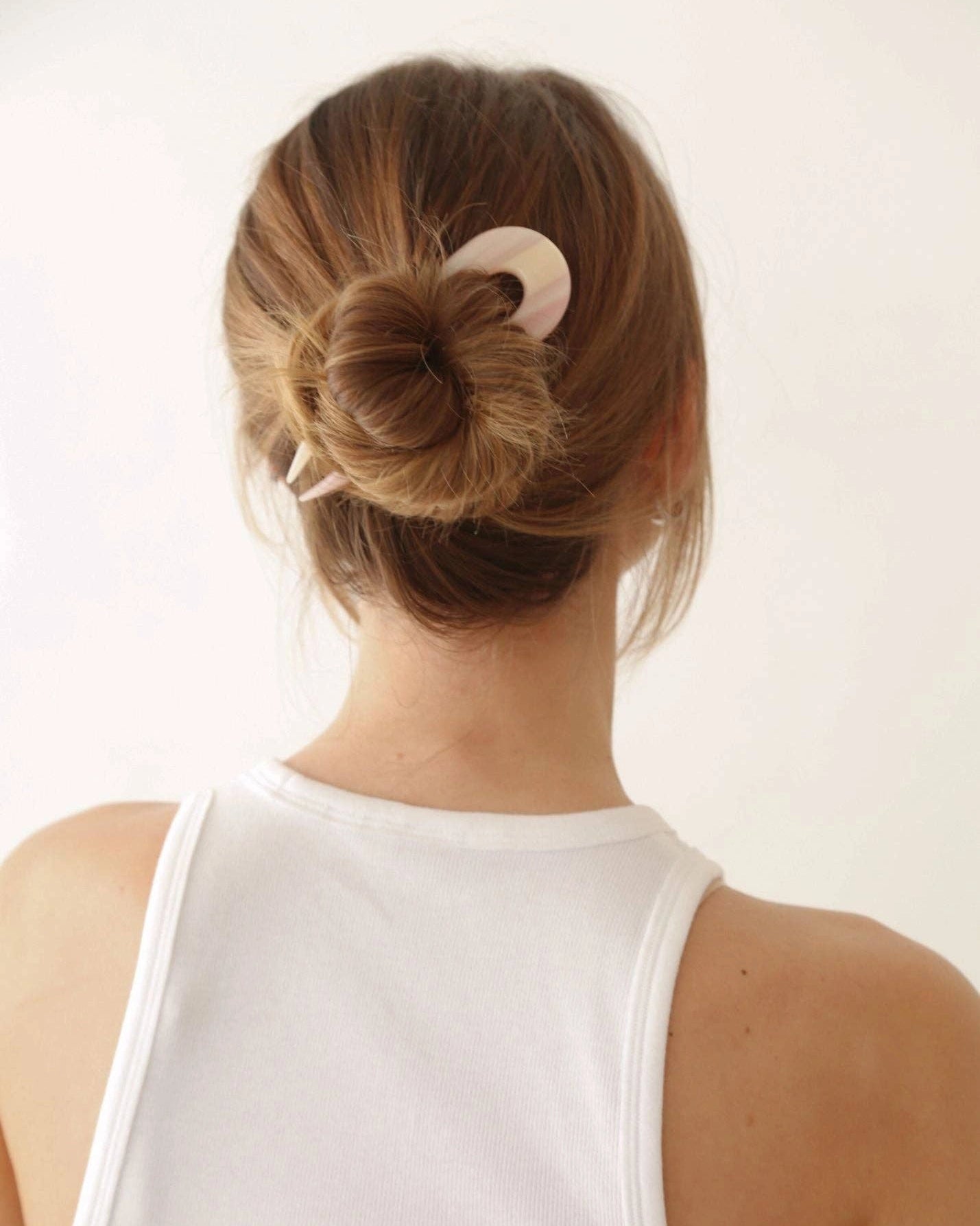 Person with a bun hairstyle using a pink French hair pin 
