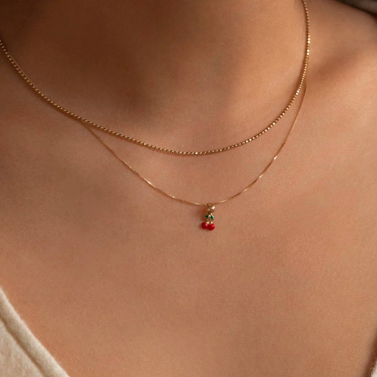 a woman wears a gold chain necklace with a cherry pendant on it by Leah Alexandra
