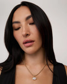 A woman wears a  gold chain necklace with a big oval crystal pendant by brand Lili Claspe