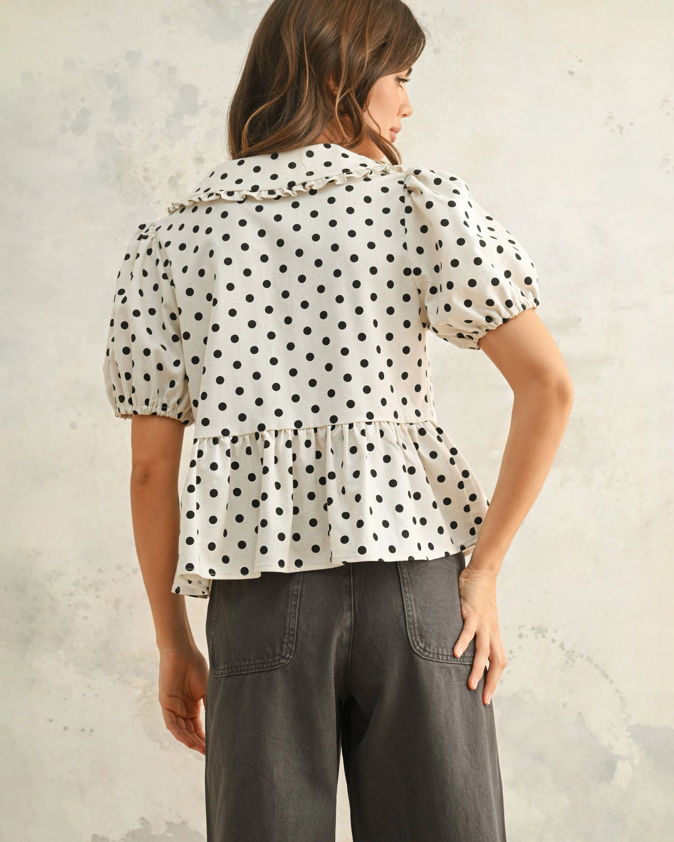 Woman wearing a white blouse with black polka dots and front ties with peplum hemline