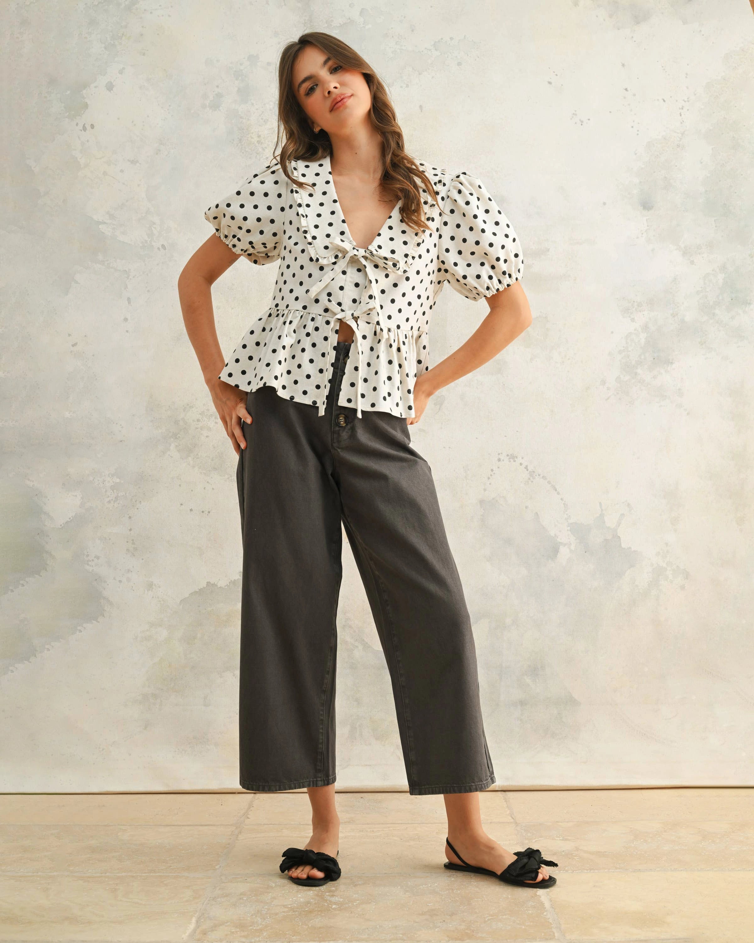 Woman wearing a white blouse with black polka dots and front ties with peplum hemline