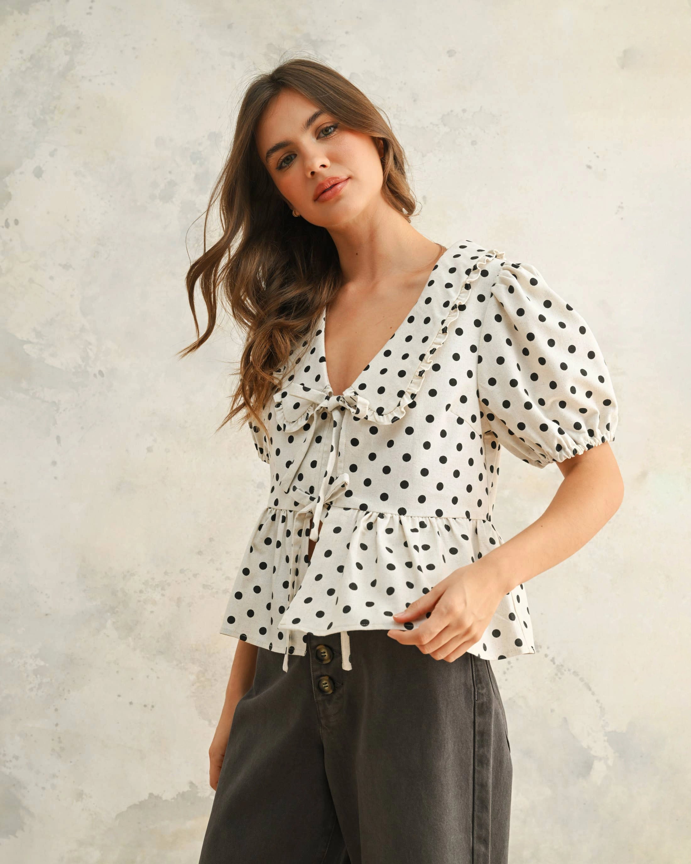 Woman wearing a white blouse with black polka dots and front ties with peplum hemline