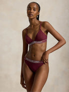 a model wears a branded triangle bralette by polo ralph lauren in a dark burgundy colour