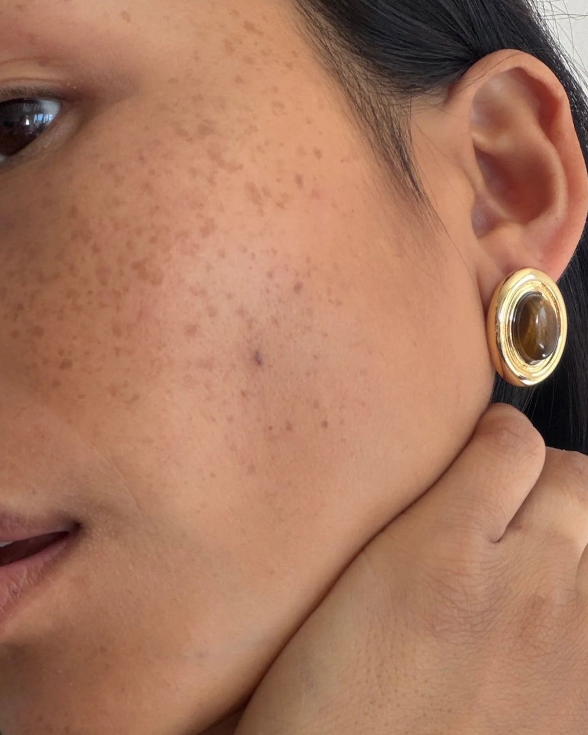 large oval earring with gold outline and brown stone in the middle
