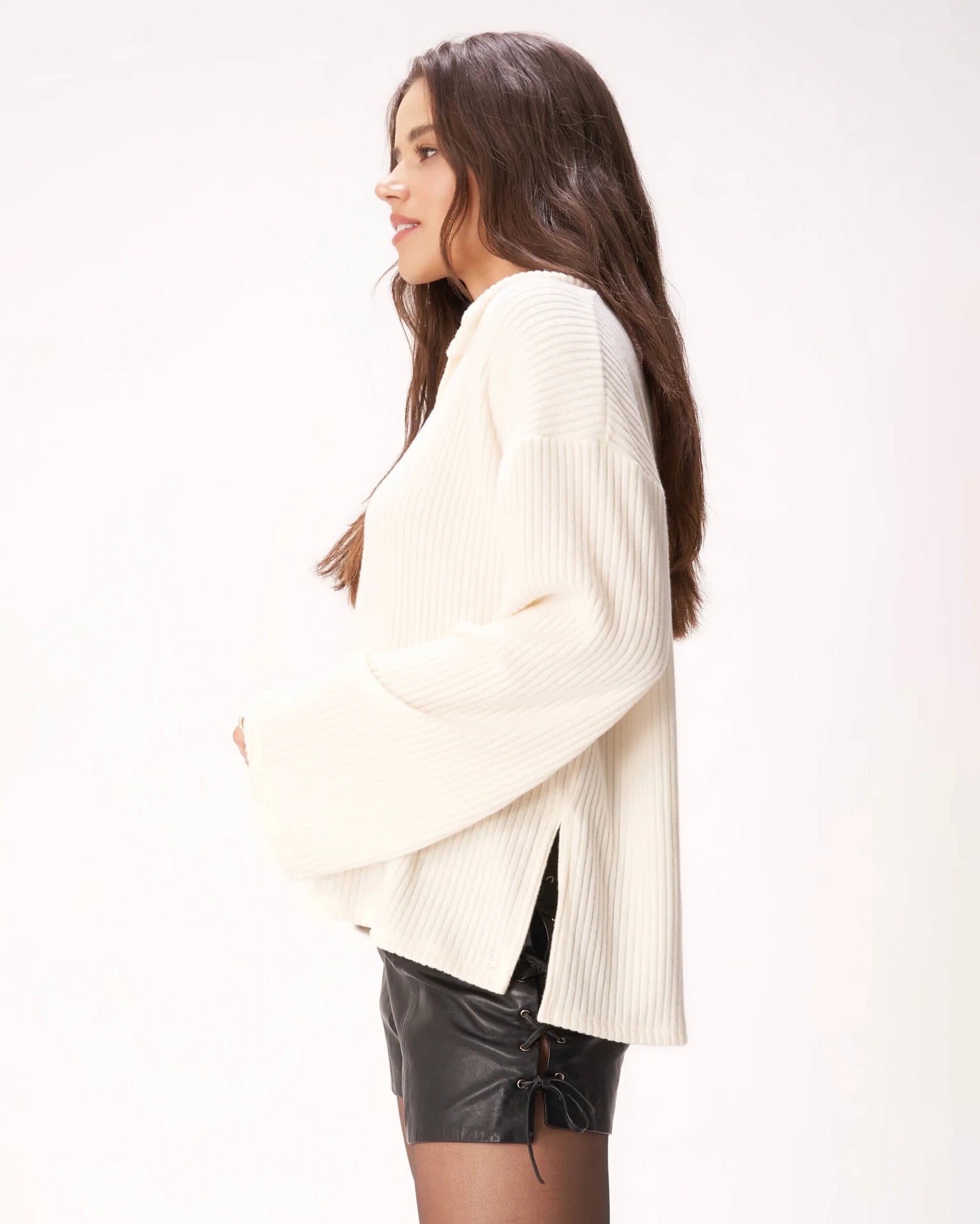 Woman wearing a ribbed cream v neck sweater and black leather shorts