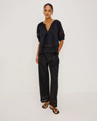 a woman wears a black cotton blouse with embroidery trim details