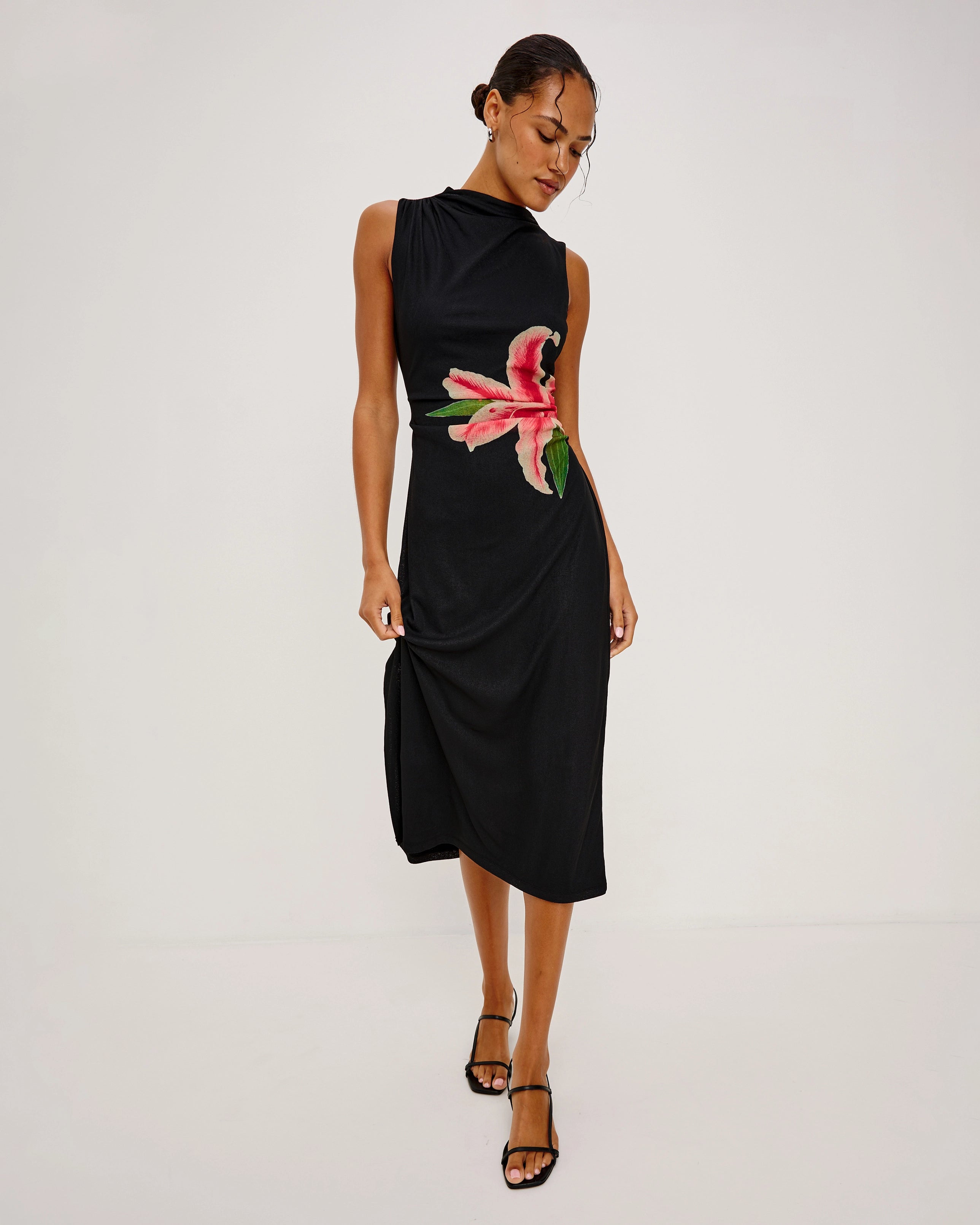 a woman wears a sleeveless black dress with a large lily on it in peach coral colour