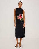 a woman wears a sleeveless black dress with a large lily on it in peach coral colour