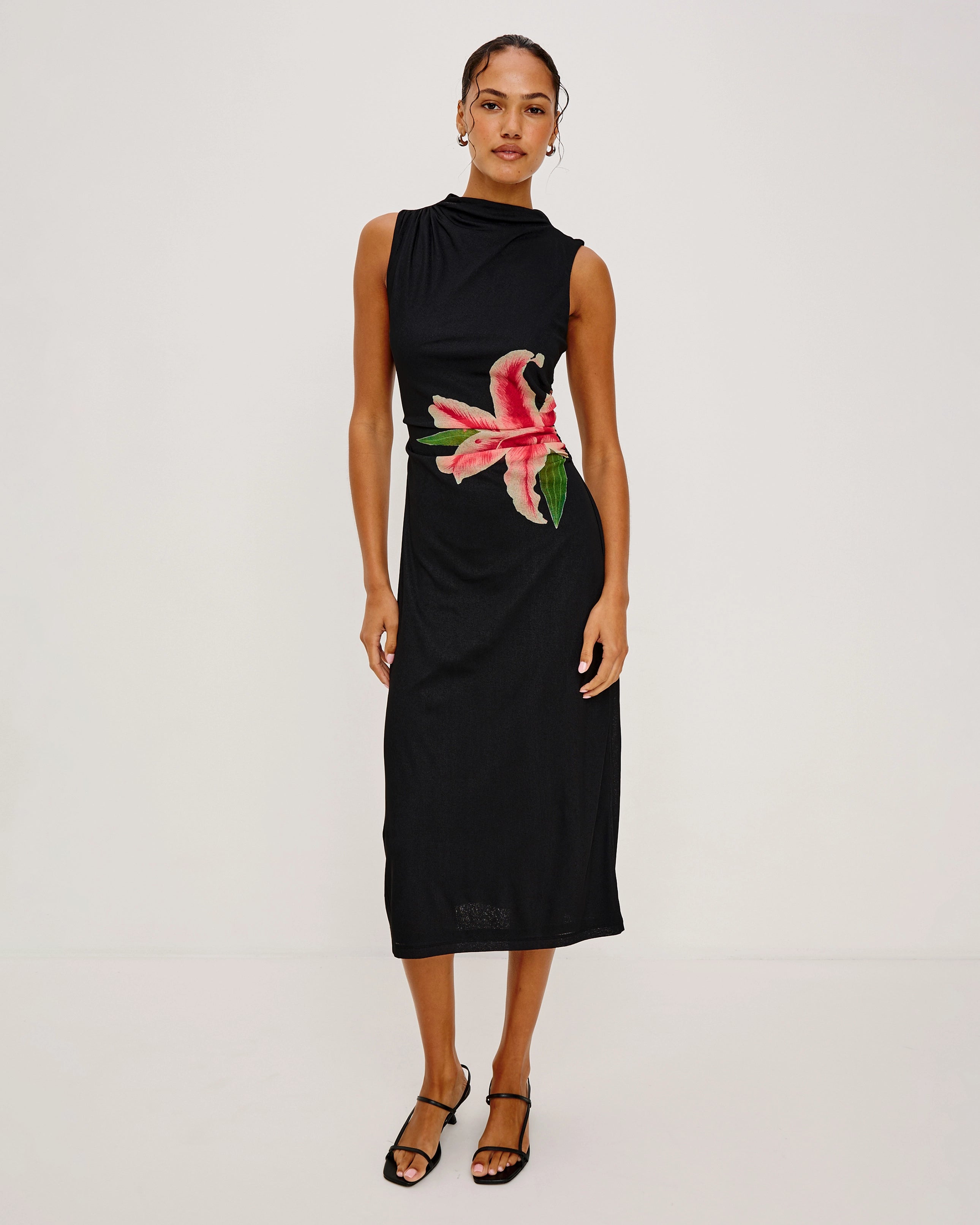 a woman wears a sleeveless black dress with a large lily on it in peach coral colour