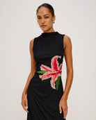 a woman wears a sleeveless black dress with a large lily on it in peach coral colour