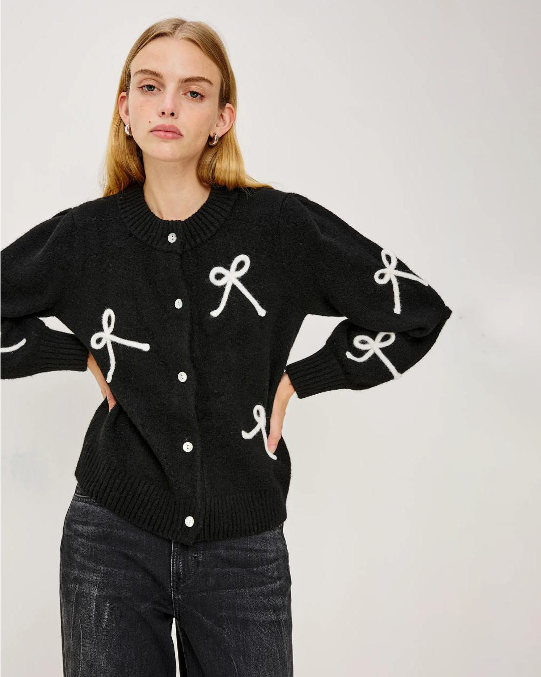 a woman wearing a black button down cardigan with white bow patterns 