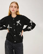 a woman wearing a black button down cardigan with white bow patterns 