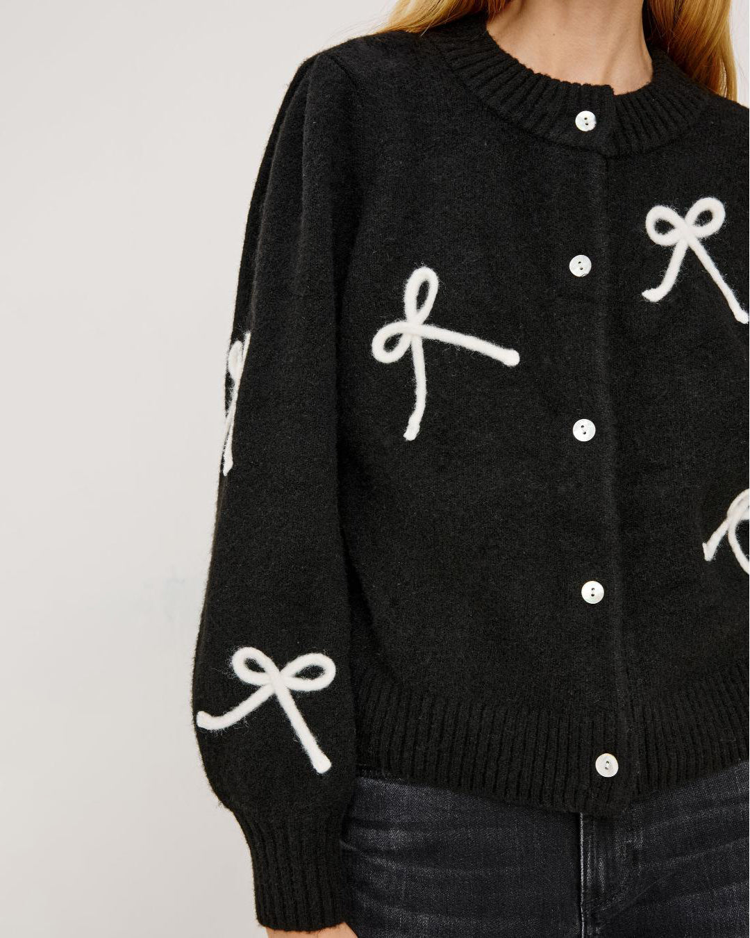 a woman wearing a black button down cardigan with white bow patterns 