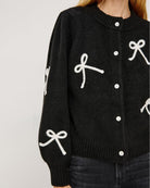 a woman wearing a black button down cardigan with white bow patterns 