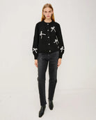a woman wearing a black button down cardigan with white bow patterns 